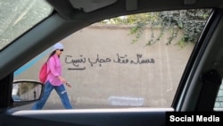 Духтари эроние аз назди деворе бо навиштаҷоти "Масъала фақат ҳиҷоб нест" убур мекунад