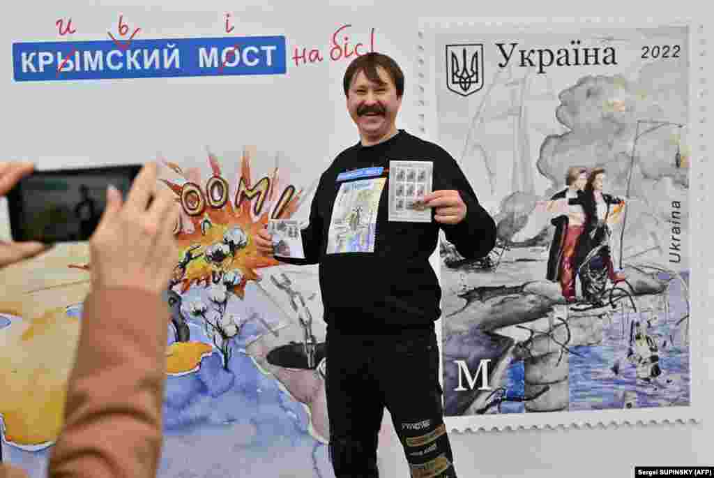 В Киеве покупатель позирует перед плакатом с почтовым конвертом и новой маркой под названием «Крымский мост на бис», в футболке с той же маркой, на главпочтамте 4 ноября 2022 года, в день начала продажи новой марки. Марку, посвященную взрыву на мосту, соединяющем украинский Крым и Российскую Федерацию, ввел в обращение почтовый оператор «Укрпочта»  