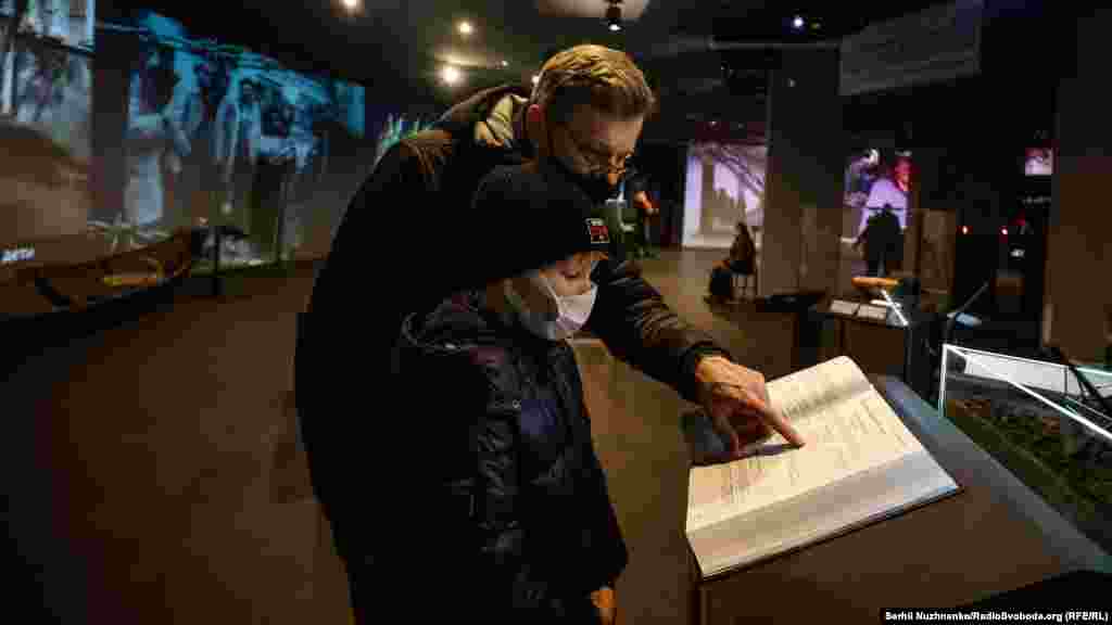 Батько з дитиною шукають у Книзі пам'яті прізвища померлих близьких