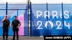 Служители на френската жандармерия стоят на стража пред ограда за сигурност, украсена с плакат на Олимпийските игри близо до Айфеловата кула в Париж, 9 юли 2024 г.