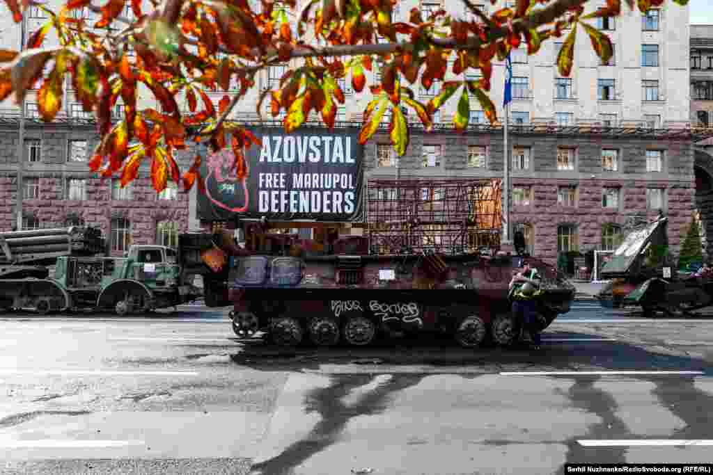 Згорілий російський БТР на тлі плаката зі закликом звільнити з полону оборонців Маріуполя та заводу «Азовсталь». Підготовка до своєрідного «параду» знищеної техніки російських загарбників до Дня Незалежності України. Центр Києва, 21 серпня 2023 року