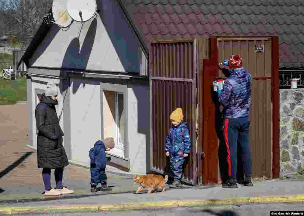 Дарія (ліворуч) дивиться, як її чоловік Максим фарбує ворота перед їхнім відремонтованим будинком. Поруч граються їхні діти. Буча, 30 березня 2023 року Рік тому на вулиці перед їхнім будинком теж лежали тіла убитих російськими військовими людей. 