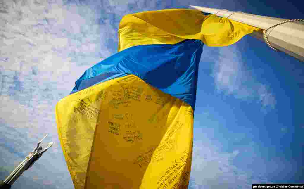 У Києві підняли прапор України з «особливими словами й підписами», які зробили на полотнищі українські захисники та захисниці. 23 серпня 2023 року (фото Офіс Президента)