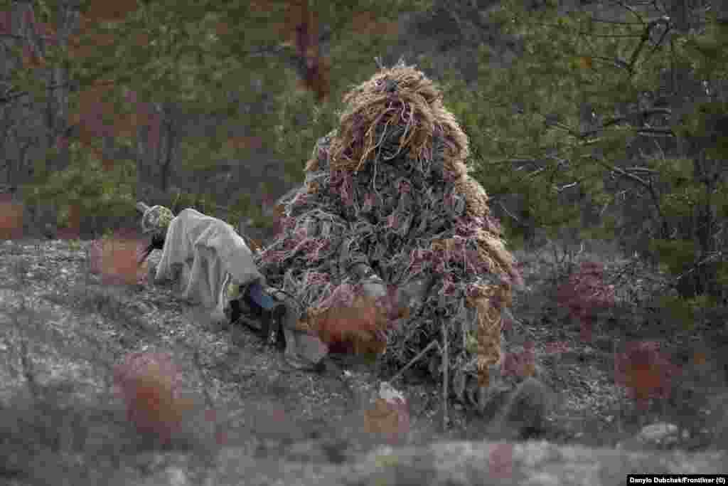 Снайперка Катерина (ім’я змінене), замаскована у «кікімору». Катерину навчають маскуванню, що є окремим мистецтвом. «Якщо ти вибрала позицію, ти не завжди можеш побачити, наприклад, свої ноги, зброю, – пояснює Катерина – Наприклад, пристебнутий ніж на поясі може блищати, потрібно це враховувати» – каже вона. Під час курсу «інструктори ходять, дивляться наші позиції, вказують на помилки, фотографують. Ми аналізуємо це все», – розповідає Катерина