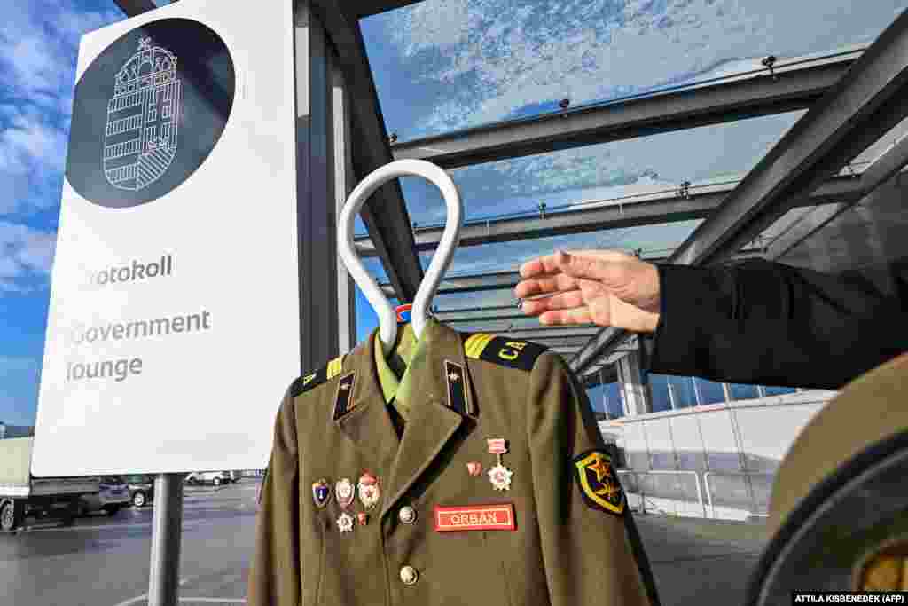 Активист венгерской общественной организации Ujratervezes («Переработка») держит руку рядом с российской униформой с надписью "Орбан" перед протокольным входом в зал ожидания венгерского правительства в аэропорту Будапешта.