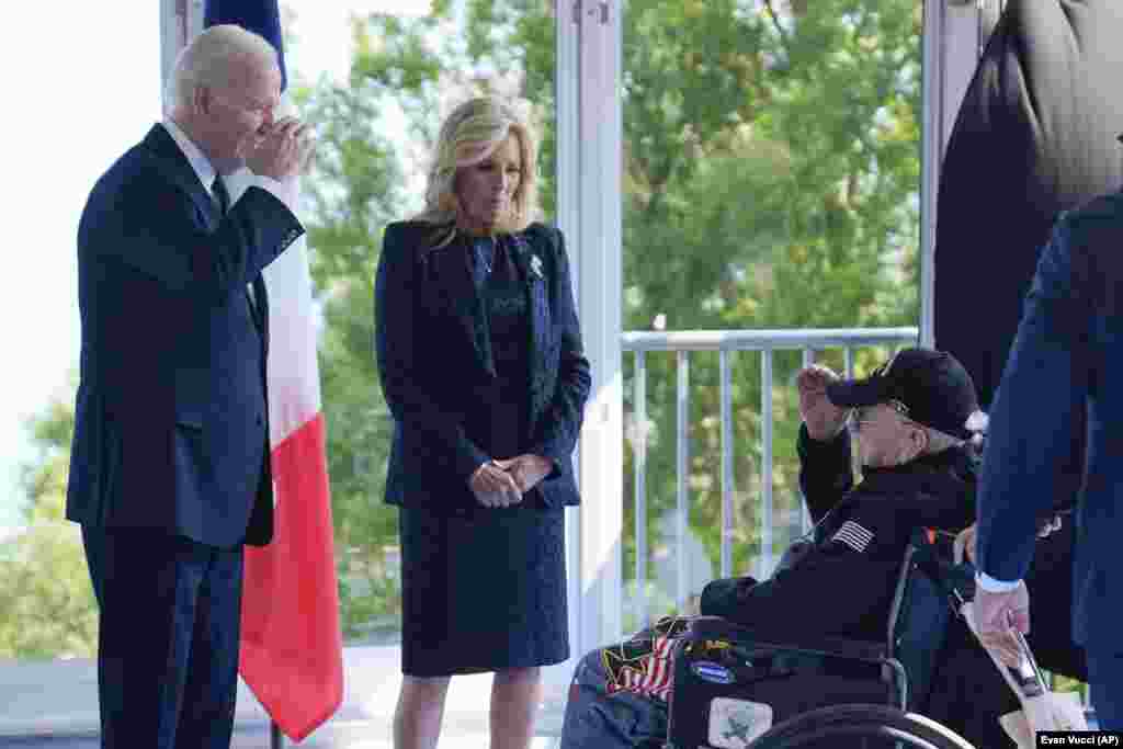 Джо Байден вітає ветерана Другої світової війни, а Джилл Байден дивиться на нього. «Ми повинні пам’ятати, що той факт, що вони були тут героями того дня, не звільняє нас від того, що ми маємо робити сьогодні. Демократія ніколи не гарантована. Кожне покоління має її зберігати, захищати та боротися за неї. Це випробування віками», – сказав Байден у своєму виступі