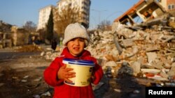 Un copil ține în mână o cutie de plastic printre dărâmături, în Kahramanmaraș, Turcia, 14 februarie 2023.
