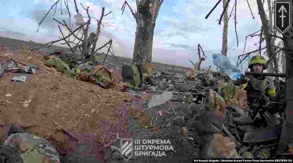 Український військовий кидає пляшку води своєму пораненому побратимові.  Фото-скріншот з відео бою навколо Андріївки на Донеччині з нашоломної камери бійця ЗСУ 3-ї окремої штурмової бригади. Агенція Reuters отримала фото 17 вересня 2023 року