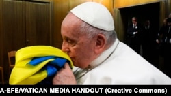 Папа Римський Франциск цілує прапор України зі знищеного армією РФ українського села, який йому подарували разом і браслетом із металу з «Азовсталі» та пачкою солі з останньої партії комбінату «Артемсіль». Ватикан, 24 лютого 2023 року