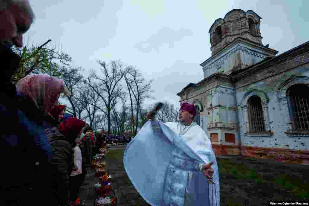 Отець Сергій кропить вірян свяченою водою на Великдень біля знищеної рік тому, внаслідок масштабного вторгнення армії РФ, церкви у селі Лукашівка Чернігівської області, 16 квітня 2023 року