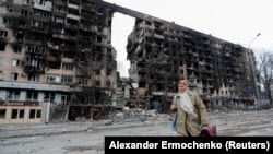 Жінка йде вулицею біля житлового будинку, зруйнованого під час штурму військами РФ Маріуполя, 14 квітня 2022 року