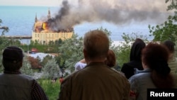 Люди дивляться на палаючу будівлю навчального закладу після російського ракетного удару по Одесі, Україна, 29 квітня 2024 року
