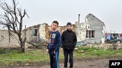 Хлопці стоять біля зруйнованої обстрілами будівлі в українському селі Новогригорівка Миколаївської області, 10 квітня 2023 року