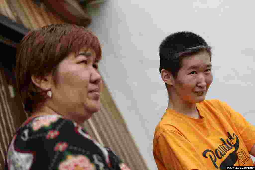 Ajman Bekmambetova (levo) i njena ćerka Ulbike u selu Han Ordasi. Ulbikeu je dijagnostikovana cerebralna paraliza i slabost mišića usled nepravilnog funcionisanja mozga. Ajman veruje da je zatrovano okruženje moglo da utiče na razvoj njene ćerke. Ulbike ima 28 godina, ali se ponaša kao dete. Igra se igračkama i nosi pelene. Ajman kaže da su komšije imale ćerku sa sličnom dijagnozom i da je umrla. Ranije je, prema njenim rečima, u selu bilo "mnogo" takve dece.