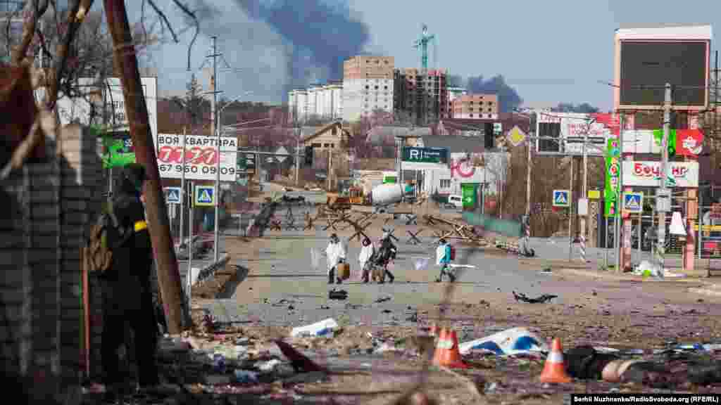 Люди йдуть із Бучі, тоді окупованої російськими військовими, фото від 11 березня 2022 року. Праворуч – фото, зроблене у травні 2023 року