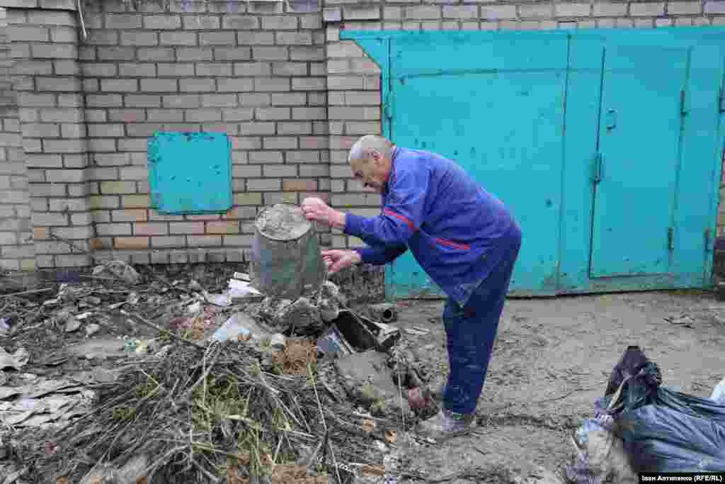 Микола виносить сміття і мокрий ґрунт зі свого будинку на вулиці Приозерній у Білозерці. Його будинок був під водою декілька днів. За кілька місяців до цього в його будинок влучив снаряд. Тоді в результаті обстрілу загинула його донька