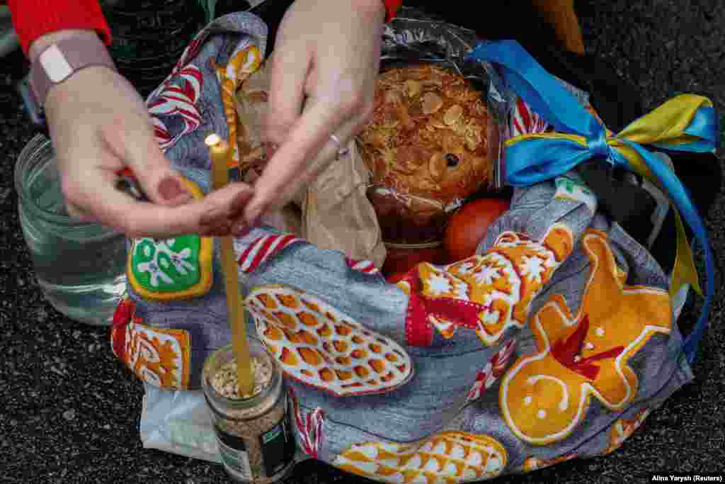 Жінка запалює свічку у великодньому кошику під час богослужіння у Володимирському кафедральному соборі в Києві, 16 квітня 2023 року 