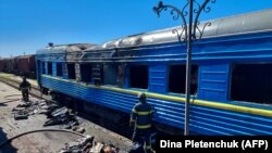 Пожежники стоять перед вагоном пасажирського потяга, пошкодженого внаслідок російського удару по Херсону, 3 травня 2023 року
