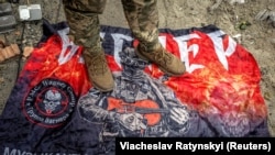 Український військовослужбовець стоїть на прапорі російської групи найманців «Вагнер» біля російського кордону в Сумській області, 13 серпня 2024 року