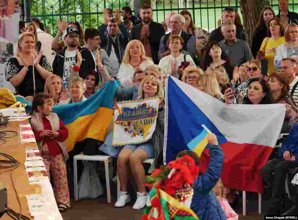 Українці на фото тримають в руках чеські та українські прапори. У Чехії проживає найбільша в ЄС кількість українських біженців з розрахунку на душу населення. Близько 339 000 українців наразі мають візи «тимчасового захисту», які дають їм можливість жити та працювати в країні