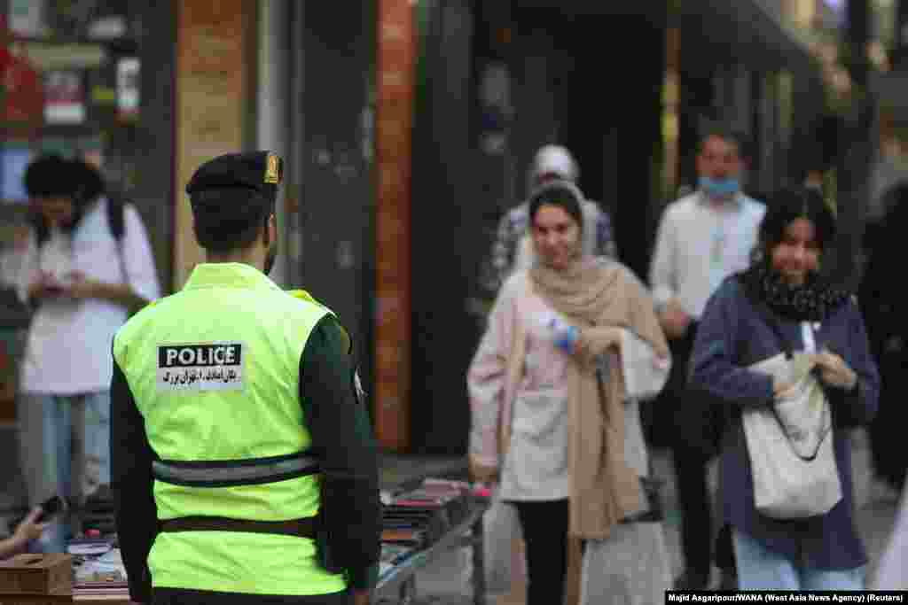 A policeman in Tehran as a woman (right) walks with her hair uncovered. Earlier this month, dozens of cafes and other businesses throughout Iran were shut down for purportedly allowing women to go uncovered.   