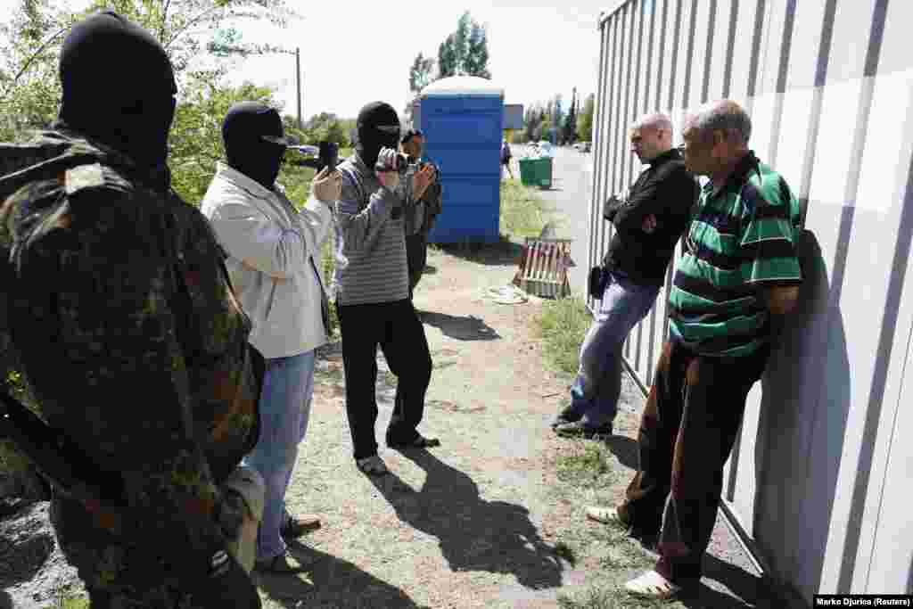 Украинские милиционеры в масках допрашивают двух мужчин на блокпосту под Мариуполем, 11 мая. Украинские войска установили блокпосты по периметру Мариуполя, поскольку ситуация в центре города в это время оставалась напряженной.