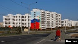 Женщина идет мимо недавно построенных домов в Мариуполе. Местные жители говорят, что новое жилье преимущественно отдают под ипотеку приезжим россиянам