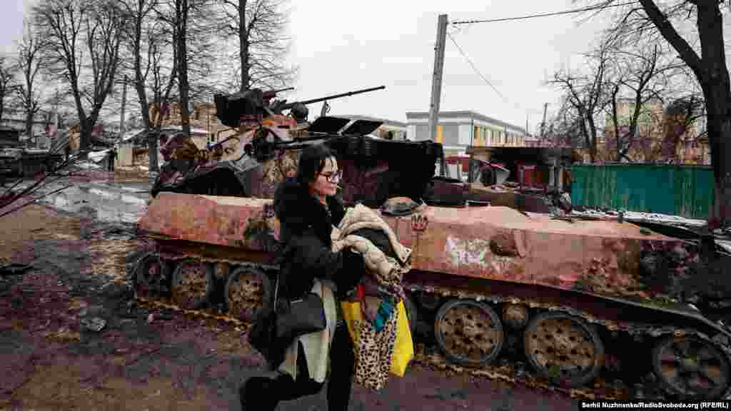 Місцева жителька Ольга: «Коли мій батько будував будинок, побудував під ним кам’яний підвал. І нам заповідав, що «якщо що, то це у вас бомбосховище». Тобто він залив там монолітну плиту. І все. Ми ці слова згадали і, звісно, облаштували там собі – постелили коврики. Спочатку добре почувалися, дивилися телевізор, іноді бігали. Потім, коли це сталося, дивимося: танки почали стріляти уже у нас у дворі. Ми уже капітально побігли у підвал, і там ми сиділи 7 годин. Танки скрипіли гусеницями, був страшний бій, а два танки заховалися за наш дім. Заїжджали до нас у доми. Танки ховалися за будинками, я так розумію. 7 годин цього кошмару: там старі і діти. Ми з життям уже попрощалися, бо над нами так ухало. А потім вийшли і побачили цю страхітливу картину. Як «армагедець» якийсь». Місто Буча, Київська область, 1 березня 2022 року. Праворуч – Ольга у травні 2023 року: «Головне, що всі живі»