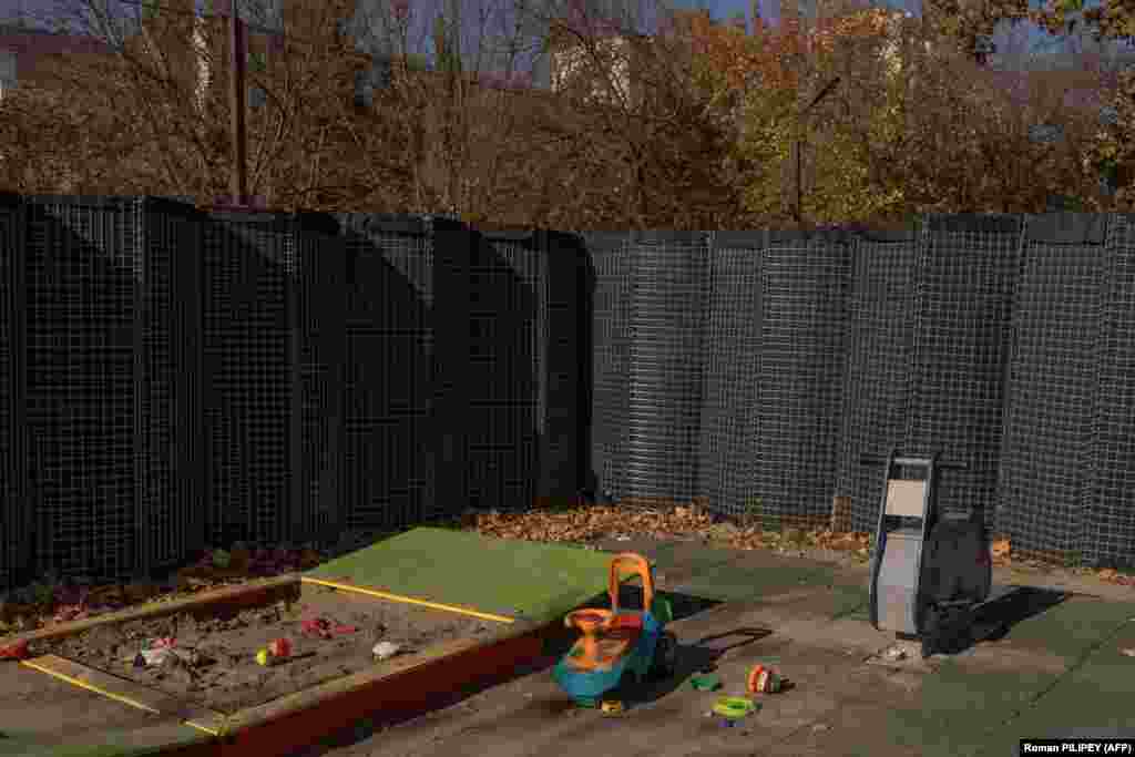 Захисний паркан від обстрілів оточує дитячий майданчик у Херсоні. Херсон розташований на контрольованому владою України західному березі Дніпра, який де-факто є лінією фронту. У міру загострення бойових дій з обох сторін батьки стикаються з важким рішенням: чи всією сім’єю сміливо витримати невпинні російські обстріли, чи відвезти своїх дітей у безпечне місце