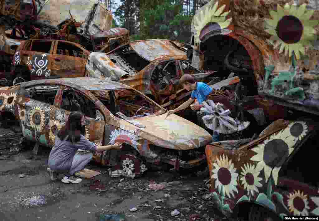 Українські художники В&rsquo;ячеслав Рибка та Олена Янко наносять фарбу на один із багатьох автомобілів, які входять до складу інсталяції. Американська благодійна організація beautifyearth.org приймає неоподатковувані пожертви для артистів, і незабаром будуть опубліковані деталі про те, де можна купити NFT. Трек Келлі каже, що інші українські міста запропонували місця для більшої кількості свого мистецтва. &laquo;Вони хочуть прикрасити ці занедбані райони, доки їх не можна буде відновити, щоб... з руїн виростала якась яскравість, колір і природа, якесь своєрідне відродження&raquo;