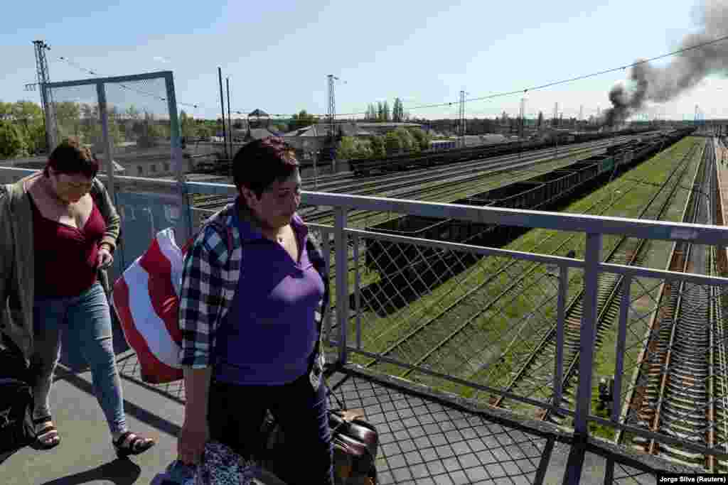 Жінки ідуть залізничним перехідним мостом біля залізничного вокзалу в Лимані Донецької області, куди перед цим прилетіли російські снаряди. У місці потрапляння розпочалася пожежа. Фото від 28 квітня 2022 року