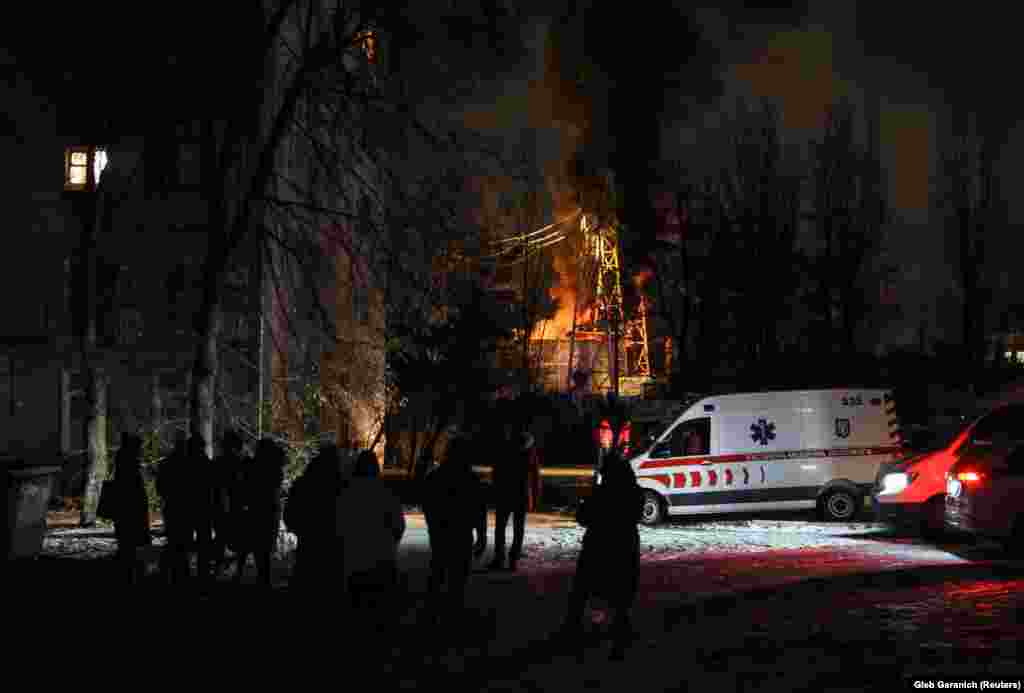 Місцеві жителі зібралися біля житлового будинку, на тлі горить об’єкт критичної енергетичної інфраструктури, як повідомила влада, після російської атаки безпілотниками, Київ, 19 грудня 2022 року