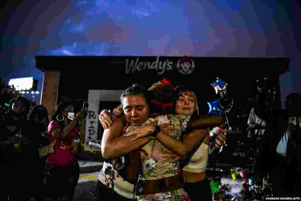 28-річна Еббі Вільямс (ліворуч) та 20-річна Аліна Фердинанд (праворуч) обіймають жінку біля спаленого ресторану швидкого харчування Wendy’s, де на парковці поліцейським був застрелений Рейшард Брукс. Атланта, штат Джорджія, США
