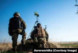 Українські військові тренуються із безпілотниками перед початком повномасштабного вторгнення Росії в Україну. Вони дивляться в екран, на якому в реальному часі відображається октокоптер, у той час як встановлений на тринозі передавач зв'язується з дроном