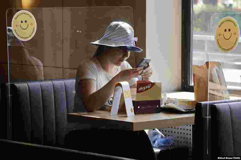 Жінка сидить за пластиковим екраном у нещодавно відкритому після карантину ресторані швидкого харчування «Макдональдс» у Москві. Росія, 23 червня