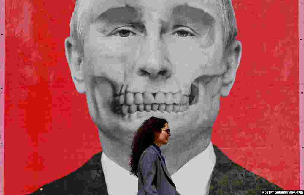 Жінка проходить повз зображення Путіна, яке висить біля посольства Росії у Бухаресті. Румунія, 29 квітня. «Спеціальна художня операція» – так називається виставка стріт-арту, де представлені роботи українських та румунських художників