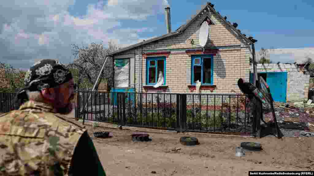 Військовий добровольчого підрозділу ЗСУ «Карпатська Січ» Андрій стоїть перед житловим будинком, пошкодженим під час російського артобстрілу. Харківська область, 2 травня 2022 року