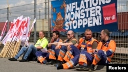 Архивска фотографија, Работници седат пред транспарент на кој пишува „Стоп на инфлациското чудовиште“ на контејнерскиот терминал Бурчардкај, додека штрајкуваат за повисоки плати во пристаништето во Хамбург, Германија, 9 јуни 2022 година.