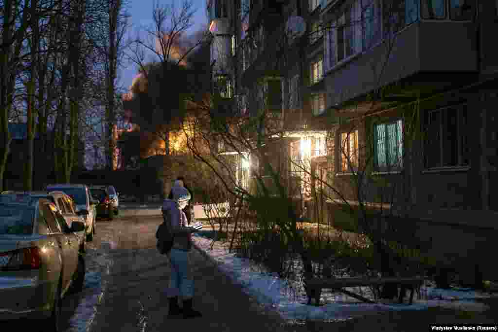 Місцеві жителі стоять біля житлового будинку, позаду горить об’єкт критичної енергетичної інфраструктури, як повідомила влада, після російської атаки безпілотниками Києва, 19 грудня 2022 року