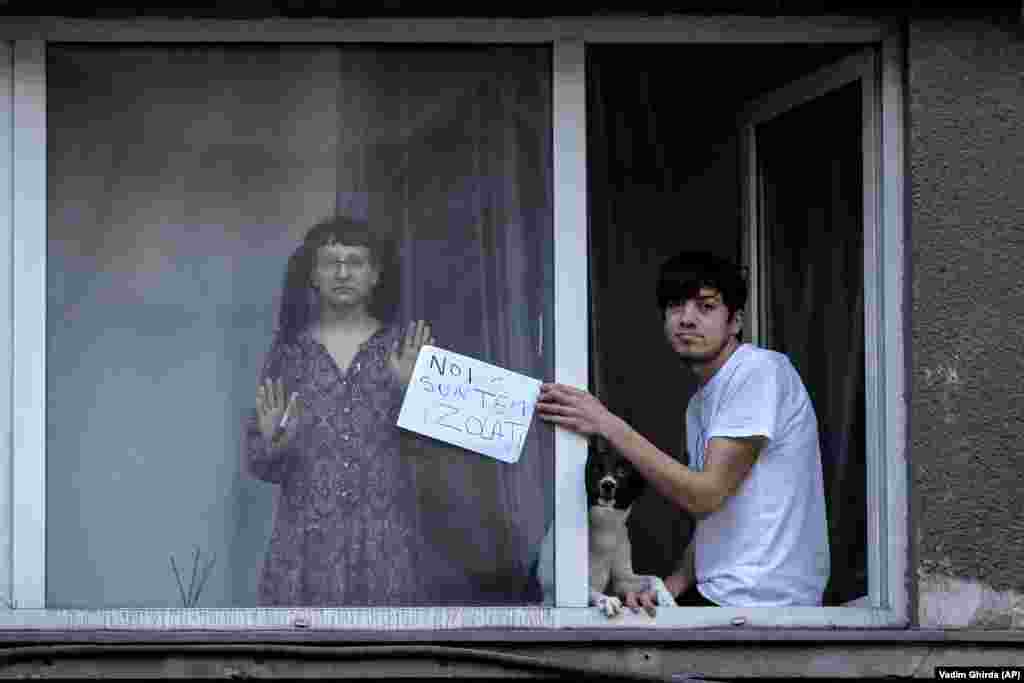 Молодий чоловік тримає табличку з написом: «Ми в ізоляції», спостерігаючи з вікна протест у Бухаресті