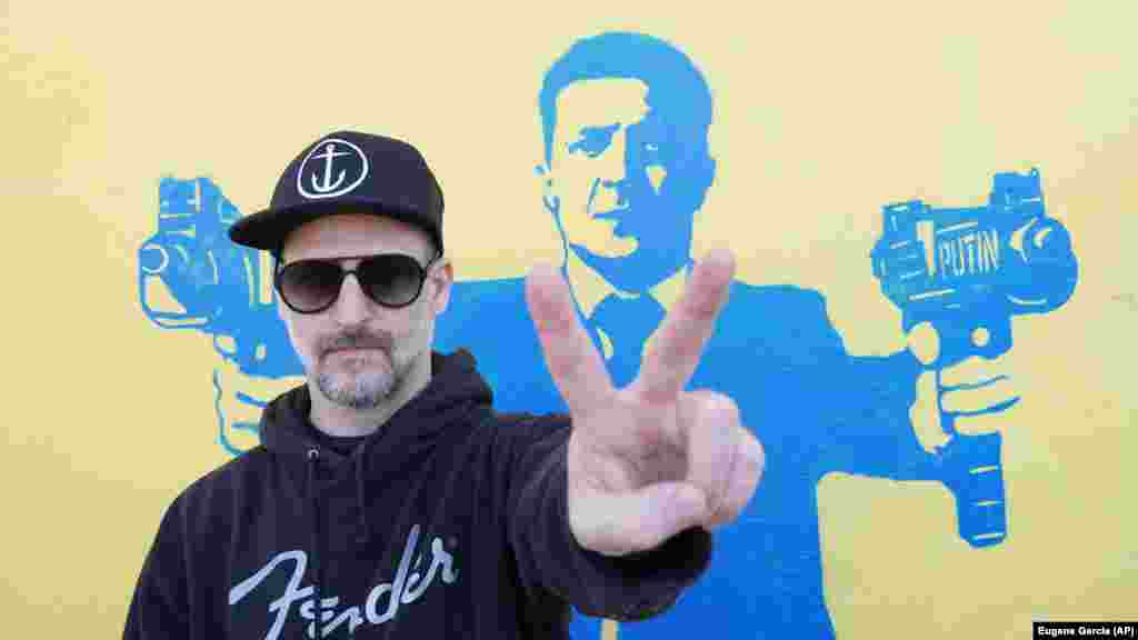 Вуличний художник Тодд Гудман, відомий як 1GoodHombre, стоїть перед зображенням президента України Володимира Зеленського.  автоматами в руках, Санта-Моніка, Каліфорнія, 21 березня 2022 року. Гудман відмовився від анонімності, ризикуючи арештом та штрафами за неліцензовану роботу зі збору коштів для українських біженців. Гудман сказав Радіо Свобода, що його роботи – заява про мирний ненасильницький опір неконтрольованій агресії та насильству Путіна в Україні. «Я гадки не маю, чи може моя робота фізично щось змінити, окрім, можливо, зміни почуття безнадійності та страху на почуття надії та хоробрості перед лицем зла»