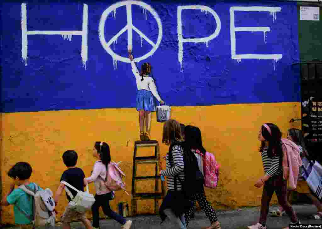 Школярі у Барселоні проходять повз мурал художника TVBOY. Дівчинка, зображена на фресці, домальовує у букві О слова HOPE (з англ. надія) символ, розроблений для британського руху за ядерне роззброєння у 1958 році, відомий як «Знак миру». Іспанія, 9 травня 2022 року