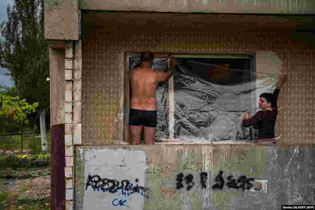 Люди намагаються затягнути плівкою вибите вибуховою хвилею вікно. Дніпро, 10 жовтня 2022 року