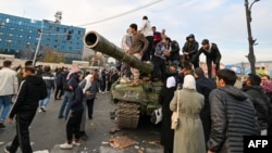 Люди стоять на танку на площі Омейядів у Дамаску 8 грудня 2024 року.