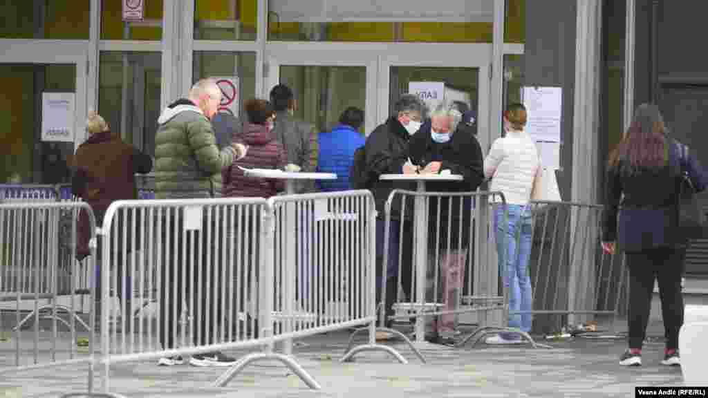 Red za vakcinaciju ispred punkta na Beogradskom sajmu (fotografija levo) nije mnogo duži nego red ispred beogradske pekare 7.oktobra (fotografija desno). Prema propisima, broj kupaca u zatvorenim objektima je ograničen, pa kupci čekaju ispred. Uredba Vlade Srbije o merama za sprečavanje i suzbijanje COVID-19 propisuje da je u redovima u javnom prostoru neophodno korišćenje zaštitne maske ukoliko nije moguće održati rastojanje od najmanje dva metra.  