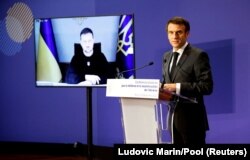 Президент України Володимир Зеленський (на екрані) слухає через відеозв’язок виступ президента Франції Емманюеля Макрона на міжнародній донорській конференції зі стійкості та відбудови України. Париж, 13 грудня 2022 року