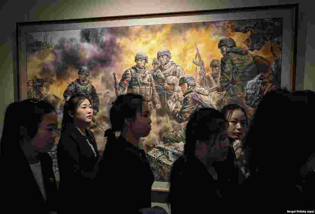 Севернокорейски туристи минават покрай картина, озаглавена "Героични бойци за достойнството и честта на родината". В горния ляв ъгъл се виждат куполите на сграда, която прилича на православна църква.