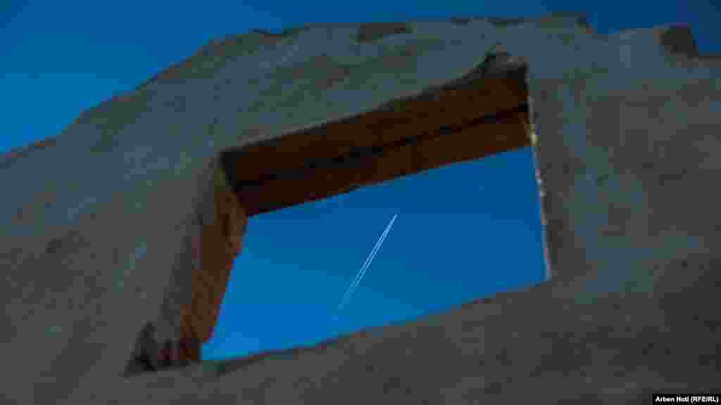 Obrisi aviona na nebu kroz prozor u zidu jedne od kuća.