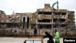 Ljudi guraju kolica kod ostataka zgrade kineske ambasade prilikom njenog rušenja u Beogradu, 2010.