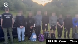 Ukrajinci za koje se sumnja da pokušavaju ilegalno preći u Rumuniju stoje u redu, dok ukrajinski graničar (lijevo) gleda u suprotnom smjeru.